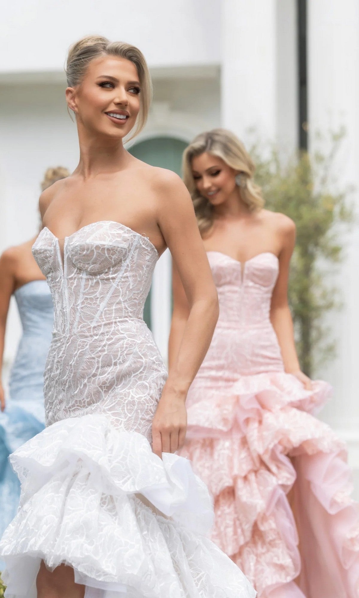 A woman walks outdoors, smiling, in the Portia and Scarlett PS25250 long formal dress in Ivory/Nude. The gown features a strapless boned corset bodice with sheer and lace detailing for elegant structure and timeless charm.